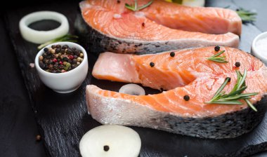 soğan, biberiye, baharat, konsept diyet, doymamış yağlar, omega 3 ile koyu taş arka plan üzerinde çiğ somon biftek
