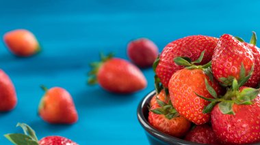 mavi bir arka planda bir kase üst görünümünde taze parlak çilek