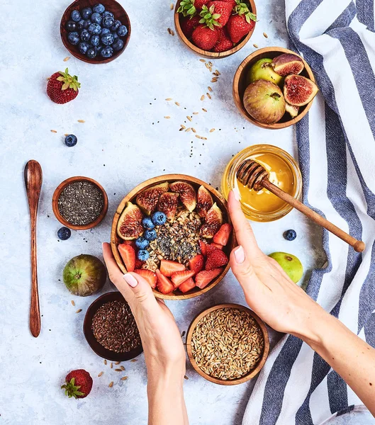 Вид сверху, показывающий, как руки едят кашу с медом, черникой, клубникой на синем фоне деревянного стола Доброе утро - здоровый фон для завтрака — стоковое фото
