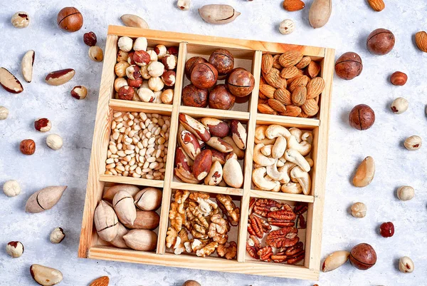 pecans, hazelnuts, almonds, pine nuts, brazil nut, cashews in a wooden box on blue background, top view, flat lay