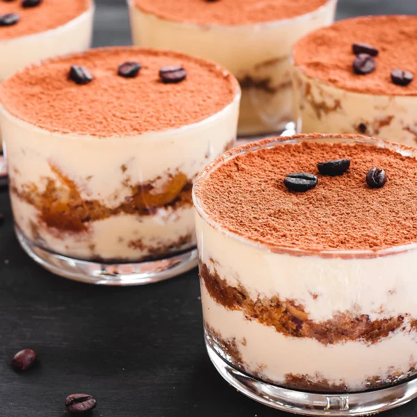 Gastronomisch Tiramisu dessert in een glas bestrooit met cacao en versierd met koffiebonen op een donkere achtergrond, luxe dessert — Stockfoto