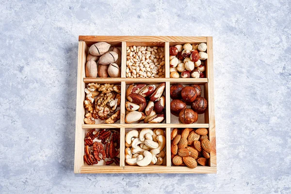 pecans, hazelnuts, almonds, pine nuts, brazil nut, cashews in a wooden box on blue background, top view, flat lay
