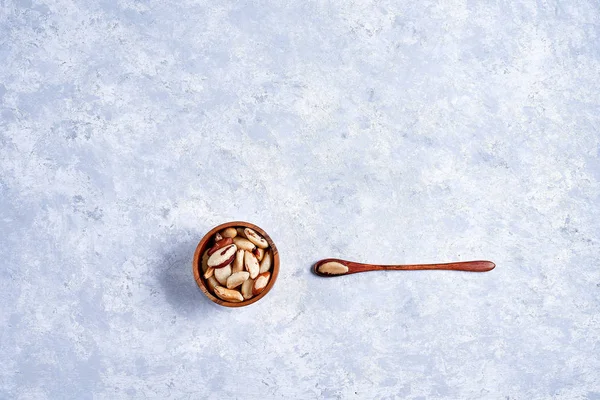 Healthy Brazil nut in a wooden bowl whith wooden spoon on a blue and white background top view — Stock Photo, Image