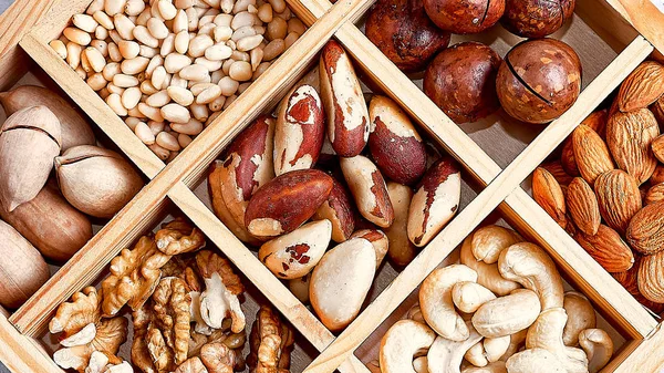 pecans, hazelnuts, almonds, pine nuts, brazil nut, cashews in a wooden box on blue background, top view, flat lay