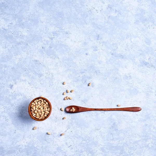 Pine nut in a wooden bowl whith wooden spoon on a blue and white background top view — Stock Photo, Image