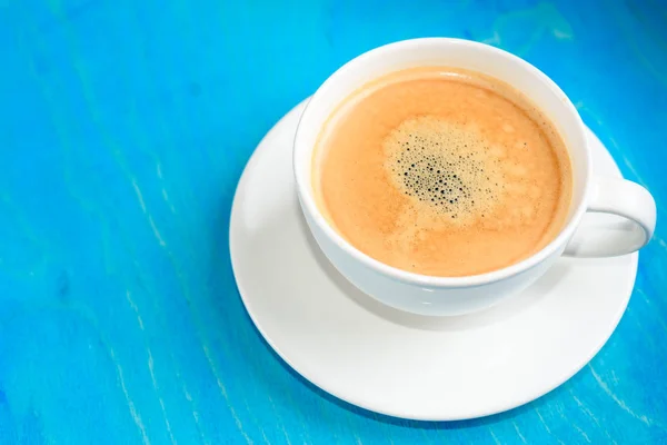 Чашка свіжої кави з піною на синьому дерев'яному фоні, вид зверху — стокове фото