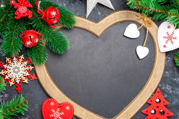 Fondo de decoraciones de Navidad o Año Nuevo: un marco en forma de corazón está rodeado por ramas de un árbol de Año Nuevo Decoraciones de Navidad, juguetes, sobre un fondo negro Copiar el espacio, vista superior, plano — Foto de Stock