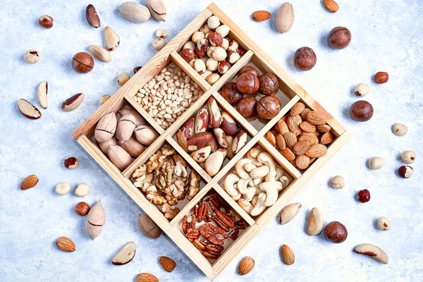 Sortiment von Nüssen in einer Holzkiste, auf blauem Hintergrund. Pekannüsse, Haselnüsse, Mandeln, Pinienkerne, Paranüsse, Cashewnüsse, Draufsicht, flache Lage. — Stockfoto