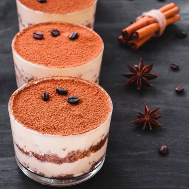 Koyu arkaplanda kahve çekirdekleri ve lüks bir tatlı serpiştirilmiş bir bardakta klasik tiramisu tatlısı.