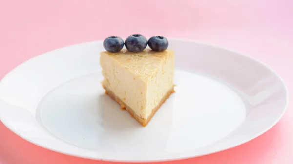 Slice of blueberrie New York Cheesecake on white plate on pink background — Stock Photo, Image