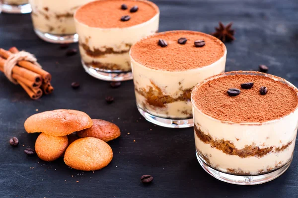 Klassieke tiramisu dessert in een glas bestrooid met cacao en versierd met koffiebonen op een donkere achtergrond, luxe dessert — Stockfoto