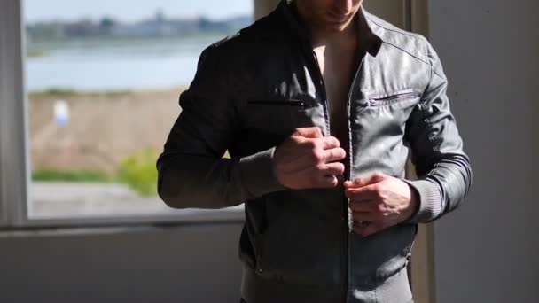 Молодий підходить чоловік, відкриваючи куртку на голому м'язовому торсі — стокове відео