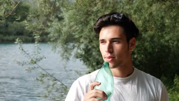 Jeune homme boire de l'eau de bouteille en plastique — Video
