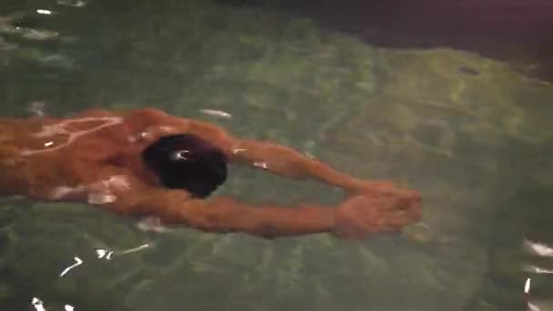 Молодой человек отдыхает в бассейне ночью — стоковое видео