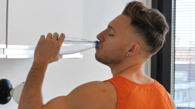 Genç adam plastik şişeden su içiyor.,