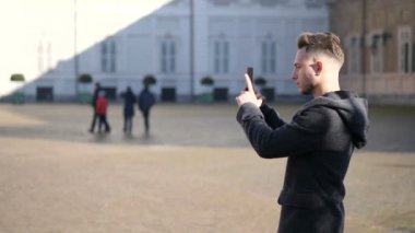 Genç adam dışarıda akıllı telefonla fotoğraf çekiyor.