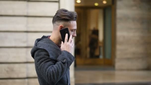 若い青電話を歩きながらスマート フォンを使用してヨーロッパの都市で目をした男 — ストック動画