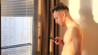 Seksi genç adam cep telefonuyla yazarak gömleksiz