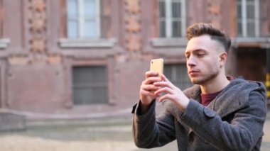 Genç adam dışarıda akıllı telefonla fotoğraf çekiyor.