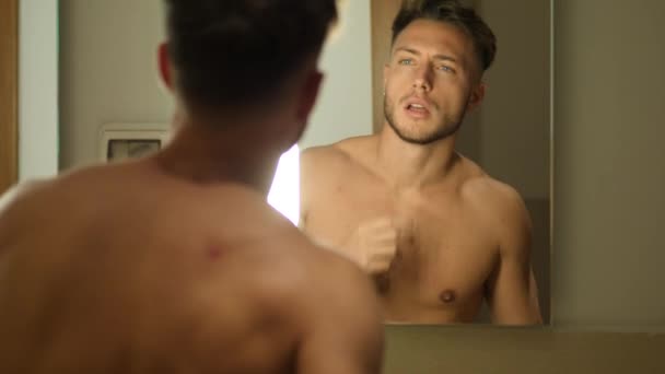 욕실에서 셔츠를 벗지 않은 근육질의 젊은 남자 — 비디오