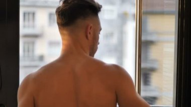 Pencereden gölgeli çizgili dalgın üstsüz adam