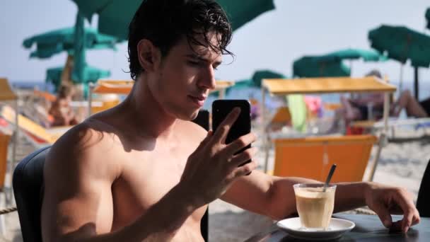 Молодий чоловік біля моря розмовляє по мобільному телефону — стокове відео