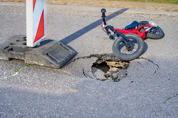 Balance bike (push bike) next to pothole on asphalt street with detour alert traffic sign