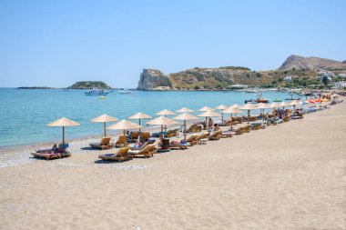 Güneş yatakları ve şemsiyeli Stegna plajı, tatilciler güneşleniyor (RHODES, GREECE) 