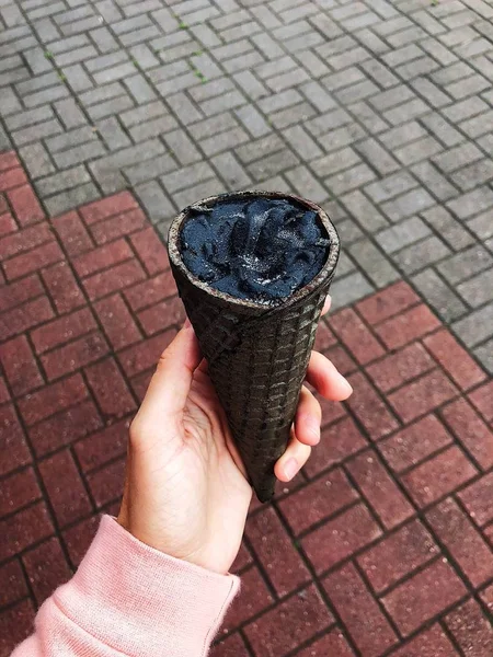 Waffle cone with black ice cream in hand