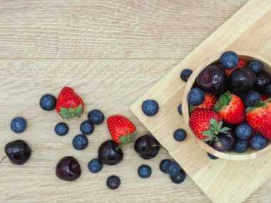 Taze yaz meyve, kiraz, çilek ve yaban mersini ahşap kase üzerinde ahşap arka plan izole.