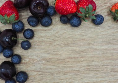 Taze yaz meyve, kiraz, çilek ve yaban mersini ahşap kase üzerinde ahşap arka plan izole.