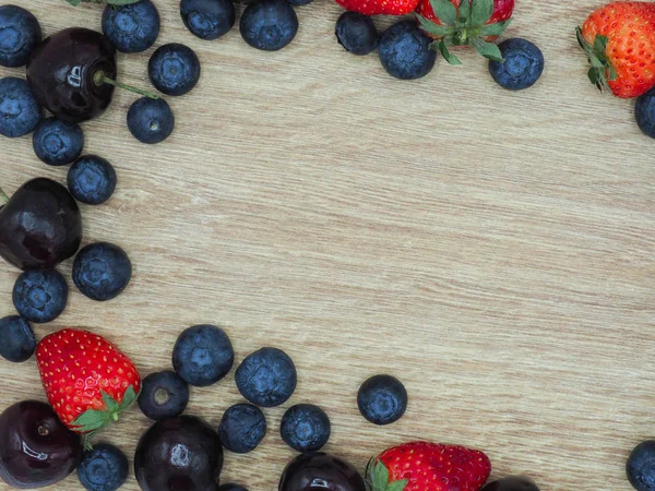 Fresh summer fruits, Cherry, strawberry and blueberry in wooden bowl isolated on wood background.