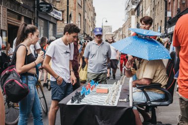 London, UK - July 22, 2018: Man playing chess with passers by in Brick Lane, London. The street is the heart of the London's Bangladeshi-Sylheti community and is famous for its many curry houses. clipart