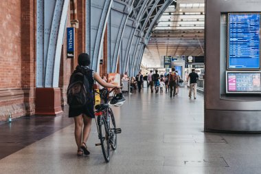 London, UK - July 26, 2018: Woman with a bike walking inside St. Pancras Station. St. Pancras is one of the largest railway stations in London and a home to Eurostar. clipart