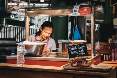 Londra, İngiltere - 17 Eylül 2018: Sıcak tuz etli sandviç Borough Market gıda tribünde, satıcı arka planda. Borough Market Londra'nın en büyük ve en eski gıda piyasaları biridir.