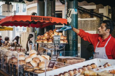 London, UK - June 24, 2018: Bread and a variety of pastries on sale at Borough Market, seller picking one up with thongs. Borough Market is one of the largest and oldest food markets in London. clipart