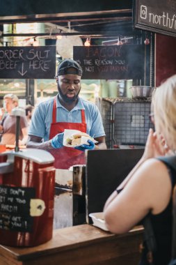 Londra, İngiltere - 17 Eylül 2018: için bekleyen kadın yemeğini Northfield kasaplık, stand Borough Market, arka plan üzerinde yemek personeli. Borough Market, Londra, İngiltere'de en büyük pazarlarından biri.