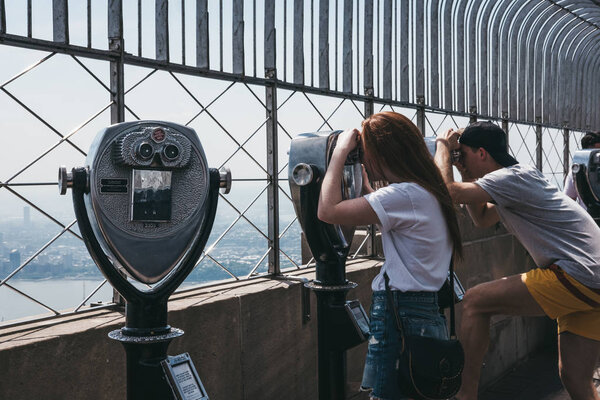 New York, USA - May 29, 2018: Visitors using binoculars on the observation platform at Empire State Building, New York. New York is one of the most visited cities in the world.