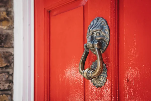 Close up of a lion's head door knocker on a bright red door of a typical British house.