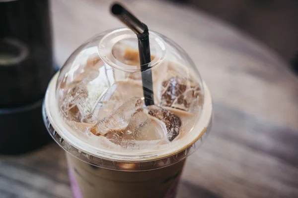 Close up of an iced coffee in a plastic cup with a straw on a table.