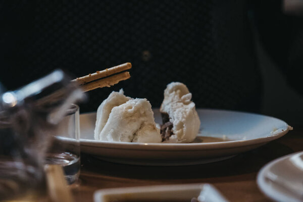 Unidentified person eating char siu bao with chopsticks.