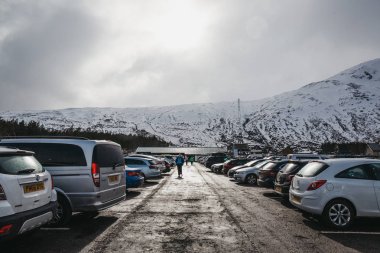 Glencoe, Scotland - March 18, 2018: People walking at the car park of Glencoe Mountain Resort. The resort located in the area of outstanding natural beauty on Rannoch Moor, Scotland. clipart
