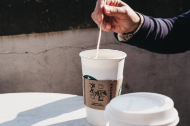 Prague, Çek Cumhuriyeti - 26 Ağustos 2018: yaz aylarında açık bir tablo üzerinde beyaz kağıt Kupası ayakta Starbucks kahve karıştırma el. Ünlü Amerikan Kahvesi zinciri Starbucks olduğunu.
