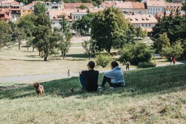 Prague, Czech Republic - August 26, 2018: Two people sitting, enjoying the view of Prague from Petrin Hill, formerly one of King Charles' vineyards and a popular place for both tourists and locals. clipart