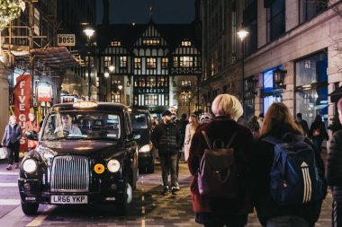 London, UK - January 05, 2019: People walking past black cabs parked on Argyll Street, London, Liberty of London department store on the background. Black cabs are an iconic symbol of London. clipart