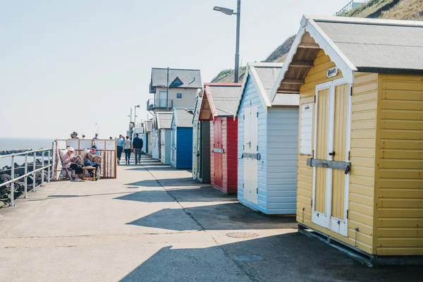 People sitting by colourful beach huts by the sea in Sheringham, — Stock Photo, Image