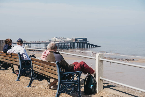 Старшие пары наслаждаются солнечным днем на скамейке у моря в Кроме
