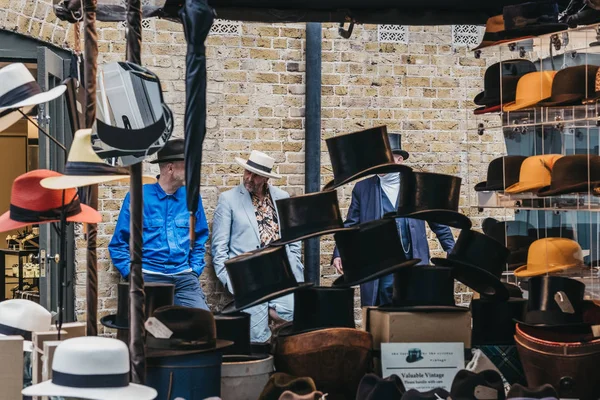 Personas detrás de sombreros a la venta en el puesto dentro del mercado de Spitalfields , — Foto de Stock