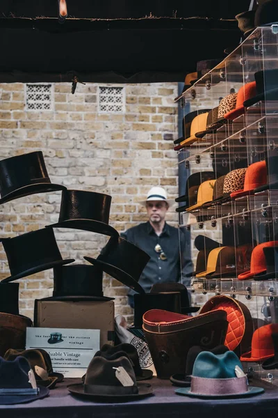 Hombre detrás de sombreros a la venta en un puesto dentro de Spitalfields Market, L — Foto de Stock