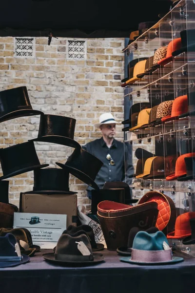 Hombre detrás de sombreros a la venta en un puesto dentro de Spitalfields Market, L — Foto de Stock